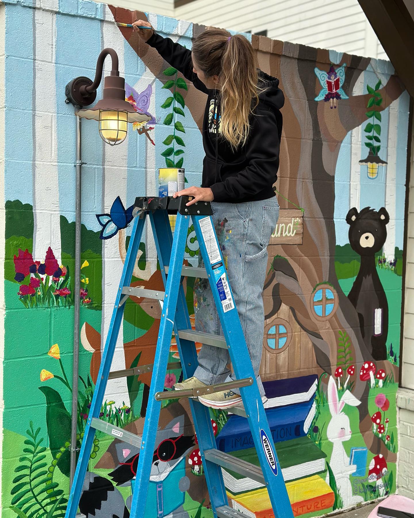 Kristen Wilson Fisher painting a forest animal mural on a ladder